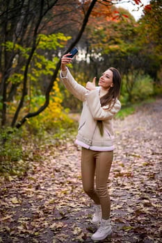 Woman taking selfie in autumn park. Young attractive lady using smartphone. photo