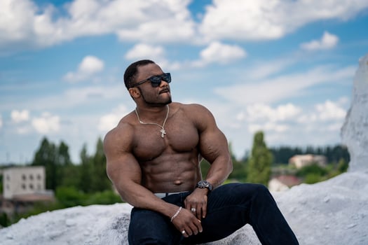 Strong topless bodybuilder model. Shirtless muscular man sitting outdoor. photo