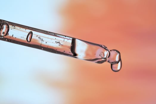 A pipette with facial serum against a sunset background in bright orange tones. photo