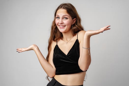 Young Woman With Brown Hair Wearing a Black Velvet Top Gesturing With Open Palms Against a White Background photo
