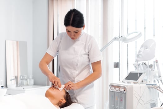 Dermatologist cleaning female client's face at bright beauty clinic photo