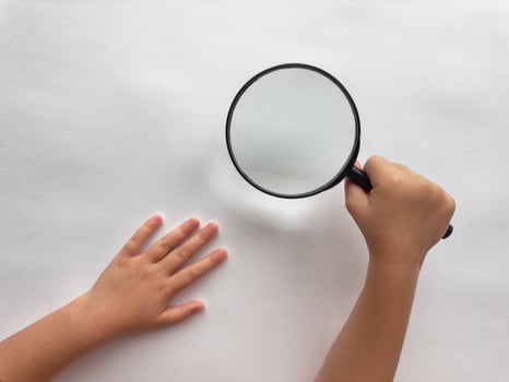 Childs curiosity. Hand holding magnifying glass over white surface photo