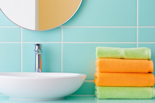 Minimalist bathroom design featuring round mirror, green towels, and bright orange accents against teal tiles photo