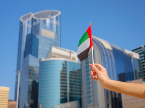 hand holding tiny flag of UAE agains city view photo