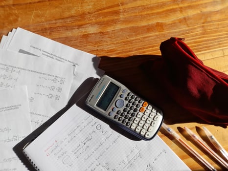 A calculator, red pen, and papers on a wooden table photo