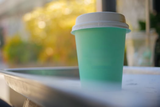 A stylish, trendy mint green disposable coffee cup sits on an outdoor table in a chic setting photo