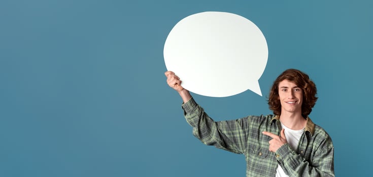 Communication concept. Cheerful curly guy pointing at speech bubble on color background photo