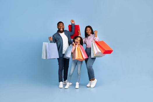 Sales And Discounts. Full length body size view portrait of African American cheerful people holding shopping bags with new clothes, family rejoice purchase, shaking clenched fists, blue studio wall photo