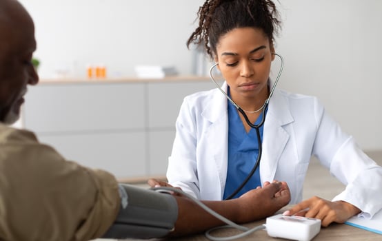Young Focused African American Lady Examining Older Patient Measuring Arterial Blood Pressure With Stethoscope And Sphygmomanometer Medical Device Sitting At Table. Hypertension Health Problem Concept photo