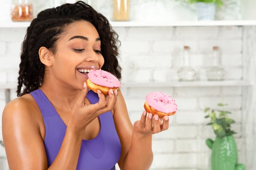 Forget About Diet. Close up portrait of a satisfied black girl eating donuts in modern kitchen, free space photo