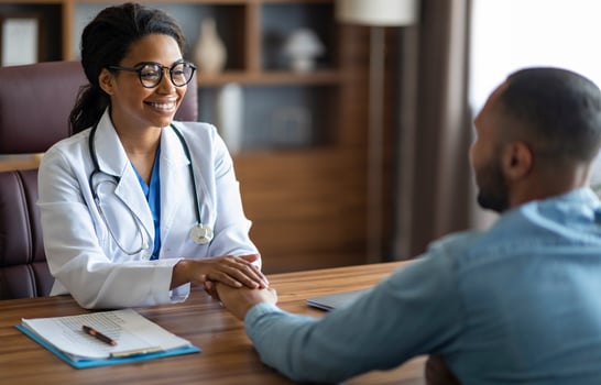 Friendly pretty young black woman in eyewear doctor holding african american guy patient hand and smiling, clinic interior, copy space. Doctor-patient relationship concept photo