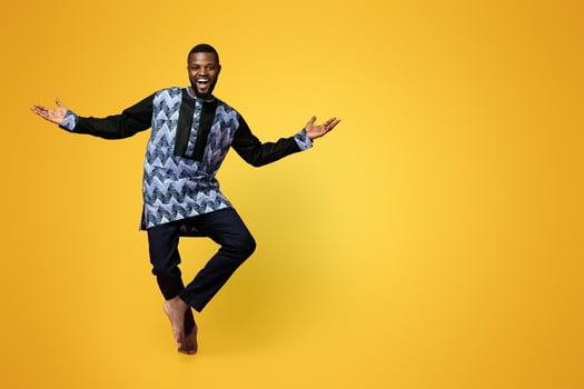 Full size photo of friendly black man dancing over pink studio background, copy space. Cheerful african american guy wearing traditional costume and showing welcoming gesture, studio shot