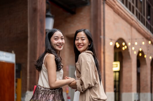 Two beautiful Asian female friends enjoy shopping together in the city, smiling at the camera. photo