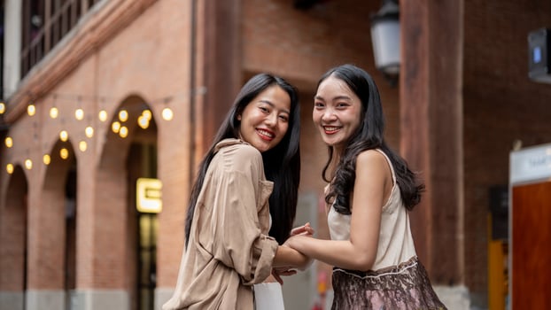 Two beautiful Asian female friends enjoy shopping together in the city, smiling at the camera. photo