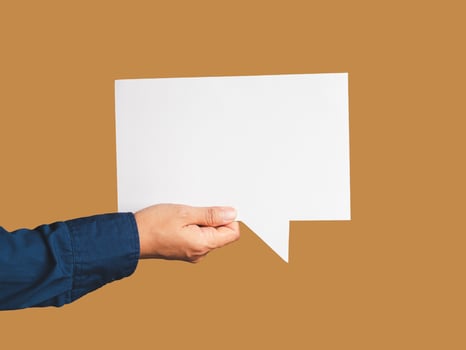 Close-up of hand holding a white speech bubble against a brown background photo