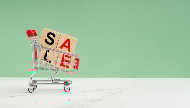 A mini shopping trolley and wooden blocks with the letters SALE over a marble floor against a green background photo