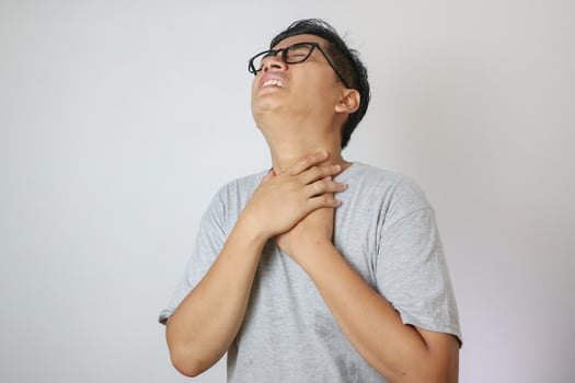 Portrait of young asian man in casual white t-shirt isolated on white background. He had a sore throat and touched his throat. Difficult to swallow. photo