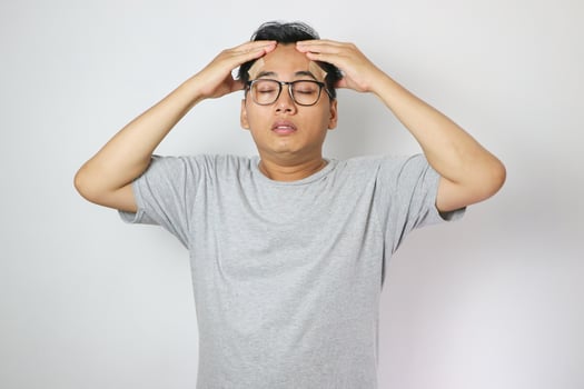 Dizzy asian young men, men headache or migraine pain suffering from vertigo while sitting on couch in living room at home, holding head with hand, health problem of brain or inner ear not balance. photo