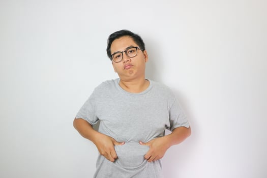 Sad Asian man wearing grey t-shirt holding pot belly. Asian man feeling full. Over weight concept. photo