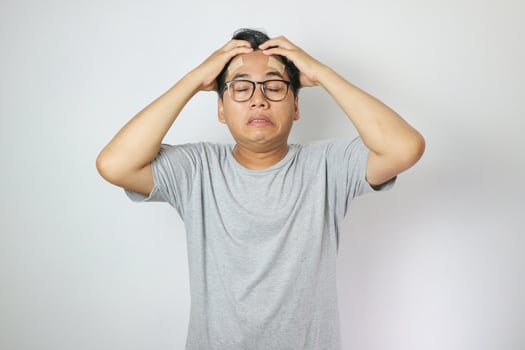 Portrait of young man isolated on gray background, suffering from severe headache, pressing fingers to temples with closed eyes photo