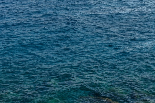 Gentle waves lap against the rocky shoreline under a clear blue sky at midday by the sea. photo