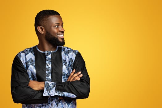 Handsome black man in traditional african costume staring at free space over pink studio background. Happy african american guy with arms crossed looking at great offer and smiling photo