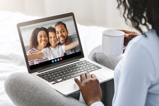 A person enjoys a call with family, smiling as they connect. The cozy atmosphere is enhanced by a warm drink while sitting comfortably on a bed in soft lighting. photo