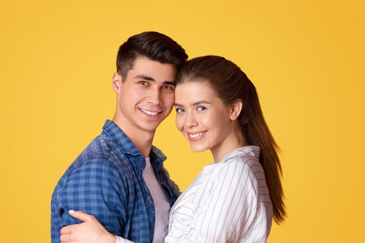 Beautiful happy couple in love and real feelings in relationships. Portrait of millennial cheerful family in casual clothes, man and woman hugging and looking at camera, isolated on yellow background photo
