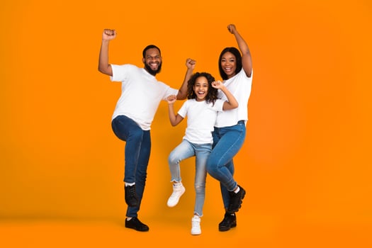 Yes. Full body length of excited young African American family of three people dancing and fooling around. Cheerful man, woman and girl celebrating win, shaking fists together on yellow studio wall photo