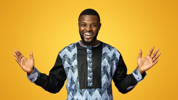 Super happy black man with arms wide open looking at camera over pink background, dressed up in traditional african costume. Emotional african american guy posing at studio, copy space photo