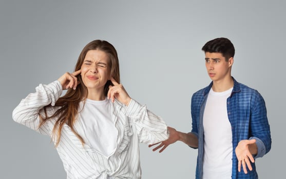 Young couple quarreling, lady covers ears with hands on gray background. photo