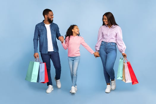 Shopping. Full body length of cheerful family of three walking together with colorful shopper bags from mall, girl holding hands with parents and talking, isolated over turquoise studio background photo