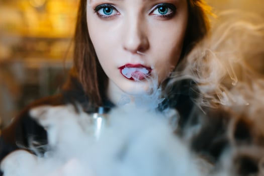 Young pretty woman in red cap smoke an electronic cigarette at the vape shop. Hip-hop style. Closeup. photo