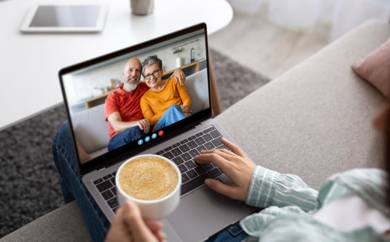 A person sits comfortably on a sofa, holding a cup of coffee and engaging in a call with family members on a laptop, promoting connection during moments of togetherness. photo