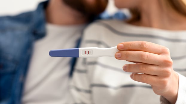 Enamoured millennial couple finding out results of pregnancy test, sitting together at home photo