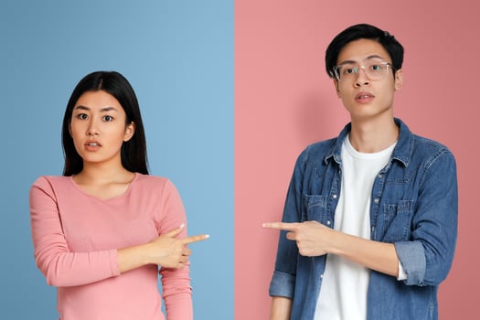 Who is guilty. Asian couple in confrontation pointing fingers at each other, grey studio background photo