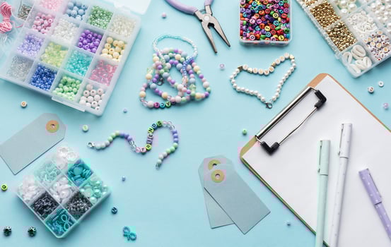 Colorful beads, pliers, clipboard and price tags arranged on blue surface for diy bracelet making photo