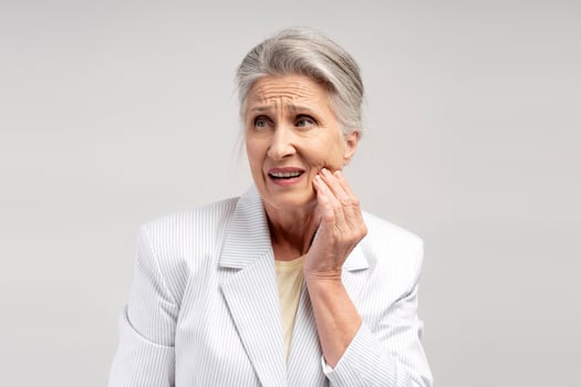 Sad, senior woman having toothache, looking away, touching cheek, isolated on white background photo