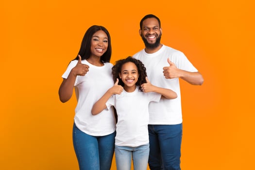 Best Choice, We Like It. Portrait of smiling black family showing thumbs up gesture with both hands, approving or recommending something good. Man woman and girl standing isolated over yellow wall photo