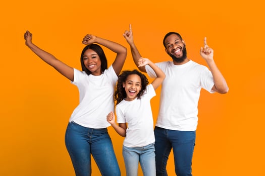 Having Fun. Portrait of excited young black family of three dancing and fooling around. Happy African American man, woman and girl enjoying favorite music together on yellow studio background photo