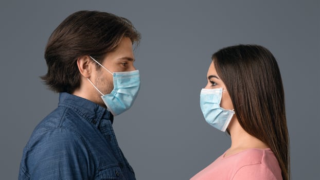 Together Against Coronavirus. Portrait Of Young Couple In Protective Medical Masks Looking At Each Other While Standing Over Light Background photo