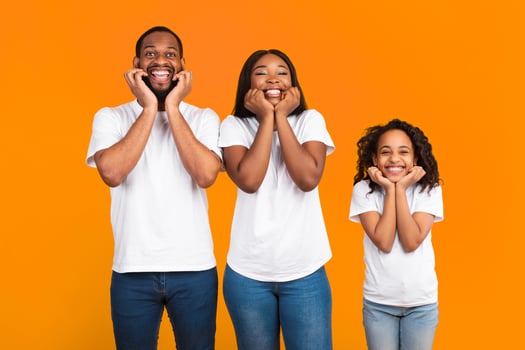 Wow, Huge Sale Or Promo Concept. Excited black family of three touching their faces and cheeks in amazement looking at camera standing isolated on yellow orange studio background. Cool Offer photo