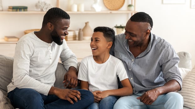 Preteen african american boy spending time at home with his grandfather and dad, relaxing together on couch in living room, chatting and laughing photo