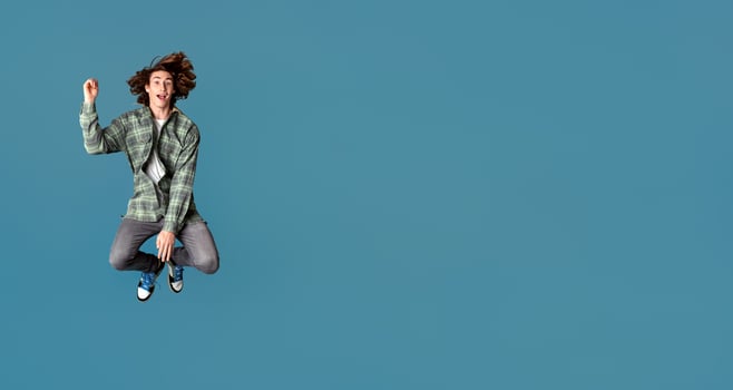 Happiness and freedom concept. Cheerful young guy in casual clothes jumping on turquoise background photo