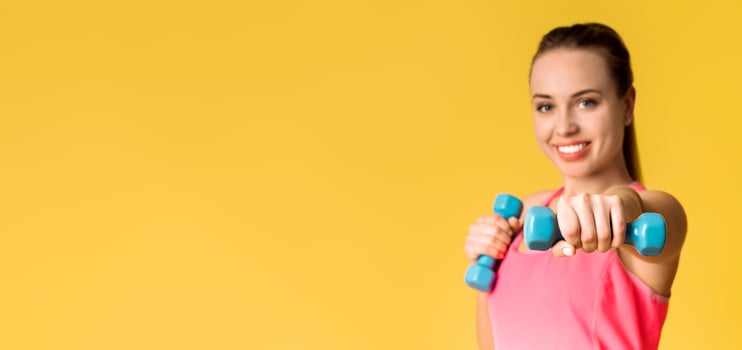 Sporty Lifestyle. Athlete Happy Woman Doing Dumbbell Boxing Cardio Workout Over Yellow Studio Background And Looking At Camera, Selective Focus photo