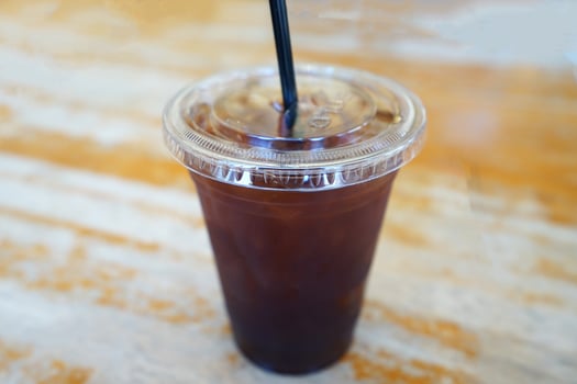 Close up take away plastic cup of iced black coffee on wooden table photo
