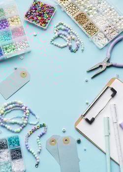 Colorful beads, pliers, clipboard and price tags arranged on blue surface for diy bracelet making photo