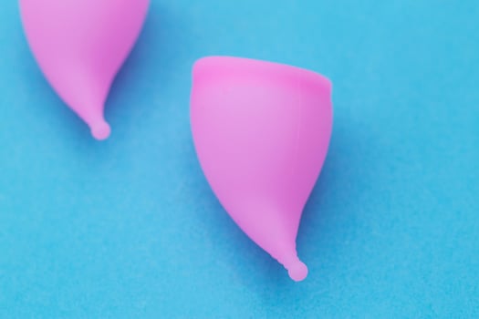 Two pink vaginal cups for girls to collect discharge during menstruation on a blue background. Replacement of female pads and tampons, close-up, gynecology photo