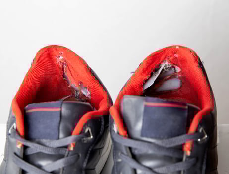 Torn backs in multicolored sports sneakers on a white background, isolate. Poor quality shoes. Copy space for text, macro photo