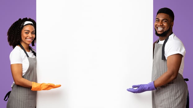 Spring Cleaning Ad. Positive African Couple In Rubber Gloves And Aprons Pointing At White Advertisement Board With Copy Space For Your Text, Panorama photo